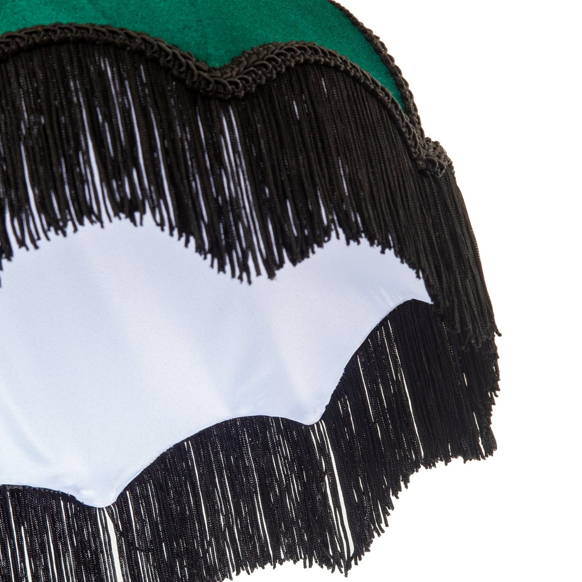 Close-up detail of a fringed garment or accessory with a green fabric top, black fringe trim, and a white scalloped section on a white background.