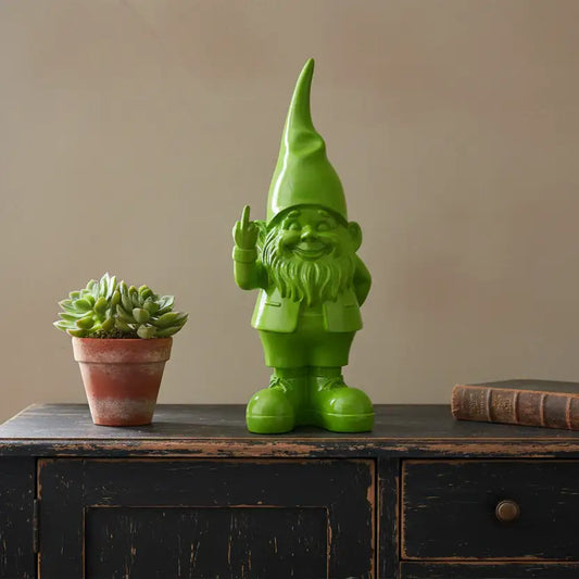 Green gnome figurine and potted succulent on a wooden surface with a beige wall background