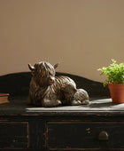 Statue of a mother bear with cubs on a wooden surface next to a potted plant.