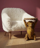 White fluffy chair and wooden lion table against a pink wall.