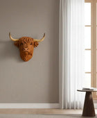 Decorative cow head mounted on a wall with a plant and chair in the foreground