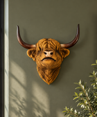 A Highland cow style bull head wall mount with long curved horns, mounted on a dark olive green wall in a styled interior setting with a window and plant visible.