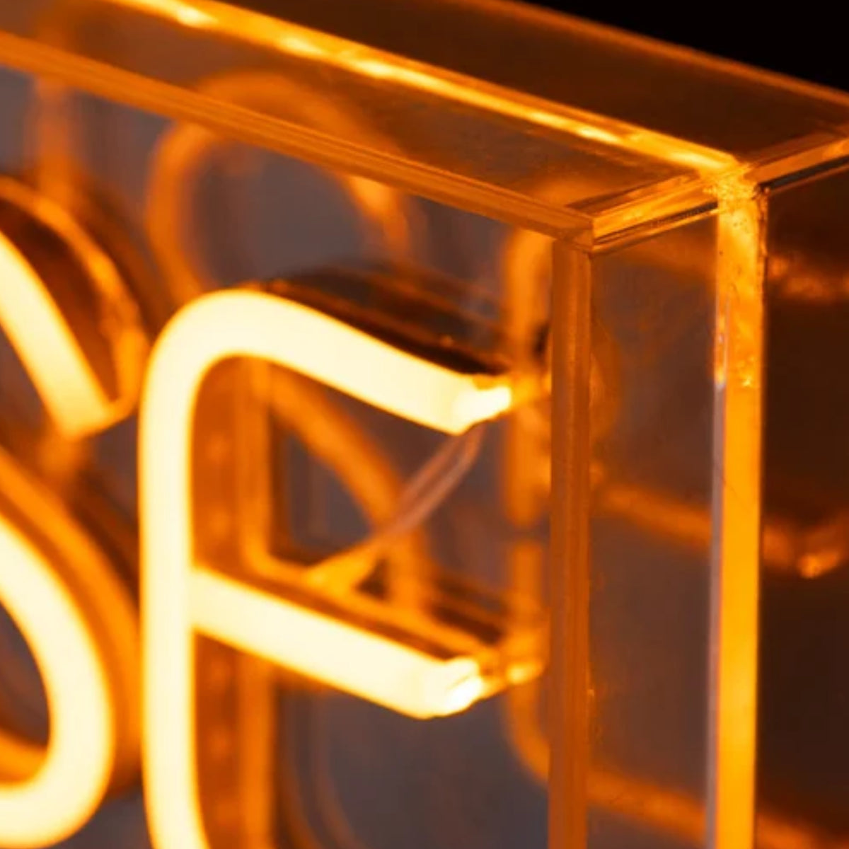 Close-up of a glowing amber neon-style sign with translucent acrylic or glass panels forming the letters 'S' and 'F'.