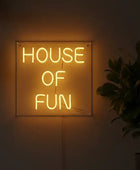 Neon sign reading 'HOUSE OF FUN' in a dimly lit room with a plant and kitchen utensils.