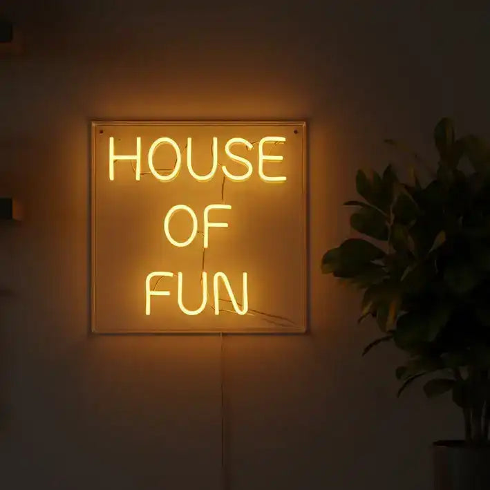 Neon sign reading 'HOUSE OF FUN' in a dimly lit room with a plant and kitchen utensils.