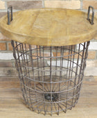 Round wooden table with metal wire basket base against a stone wall.