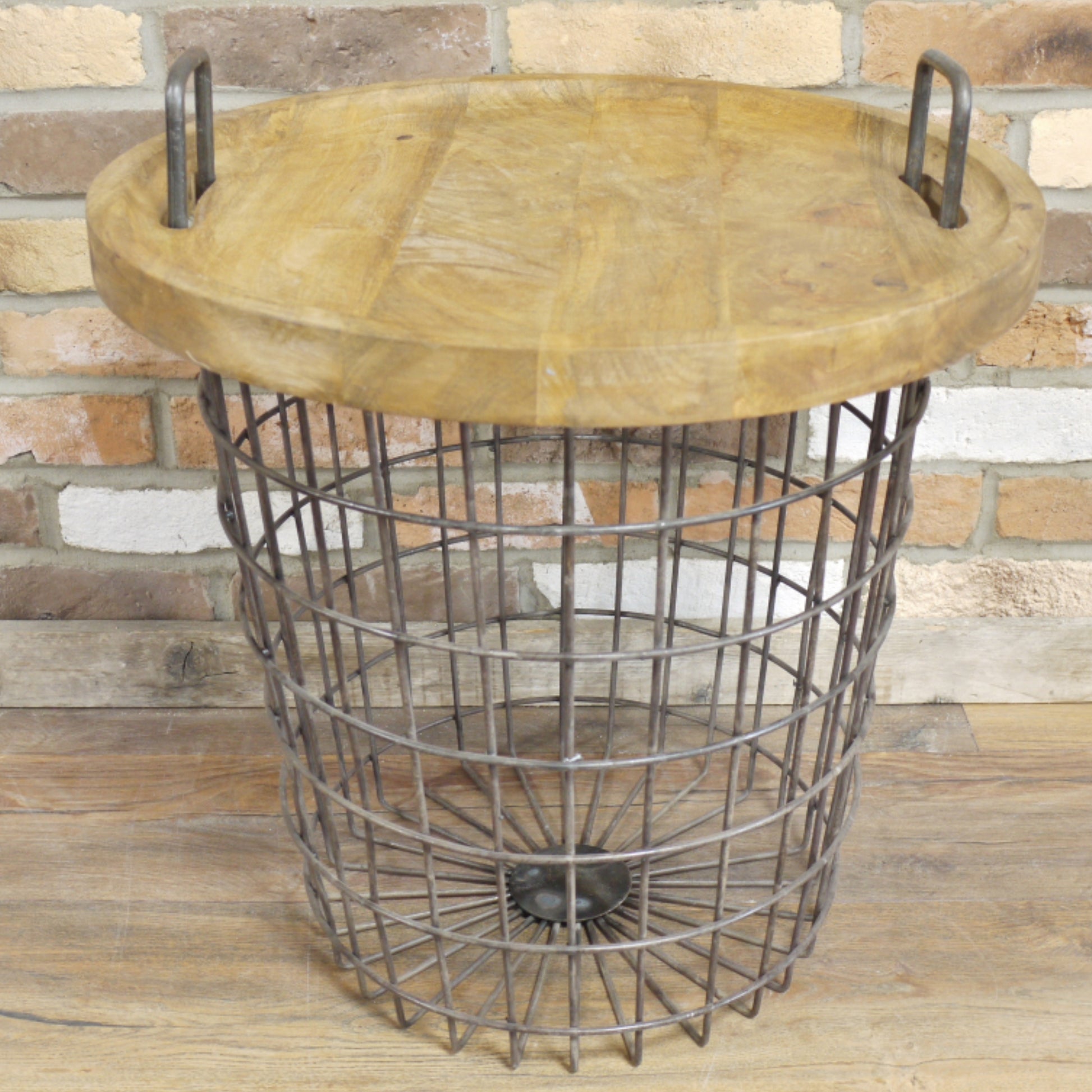 Round wooden table with metal wire basket base against a stone wall.