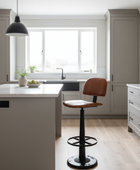 A modern kitchen island with a brown leather swivel barstool in a bright, contemporary kitchen featuring light gray cabinets and wood floors.