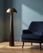 Navy armchair next to a tall bronze floor lamp in a room with a window and plant.