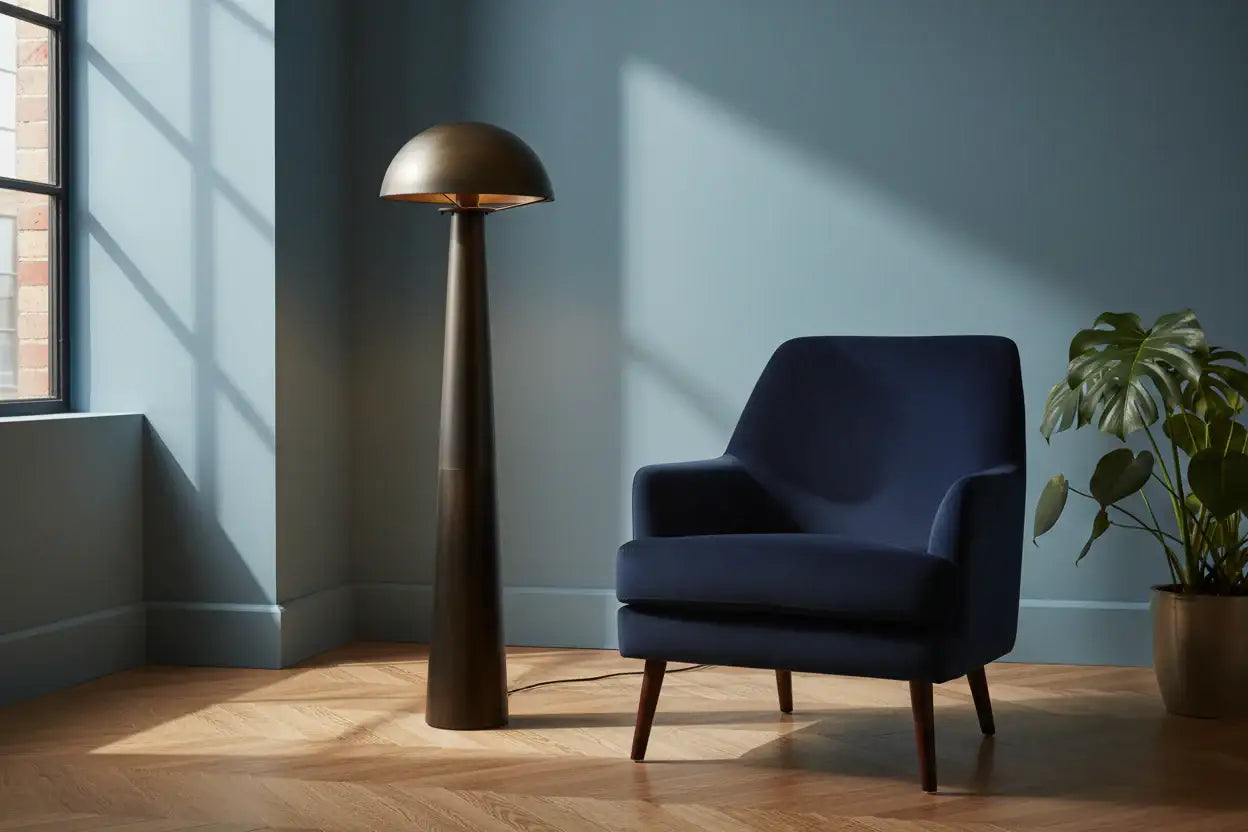 Navy armchair next to a tall bronze floor lamp in a room with a window and plant.