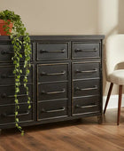 Dark wooden dresser with multiple drawers next to a white chair in a room with a plant.