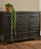 Dark wooden dresser with multiple drawers on a wooden floor, featuring a potted plant on top.