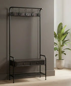 Black metal coat rack with a small table and hooks against a neutral wall with a plant.