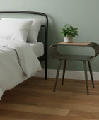 Bedroom with a bed, nightstand, and plant against a green wall.