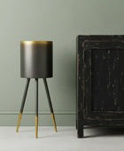 Modern black and gold tripod lamp against a green wall with a dark wooden cabinet.