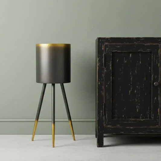 Modern black and gold tripod lamp against a green wall with a dark wooden cabinet.