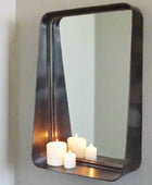 Rectangular mirror with a black frame on a gray wall, reflecting candles.