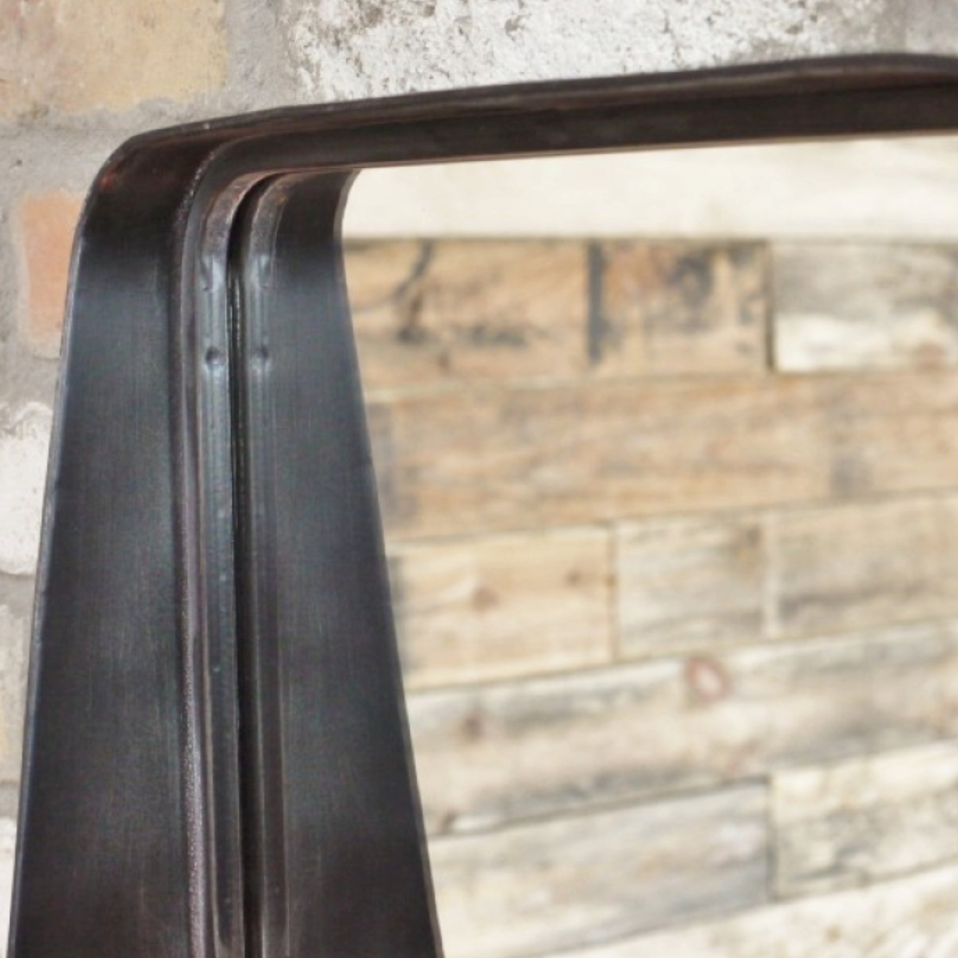 Close-up of a metal frame with a reflective surface against a textured wall.