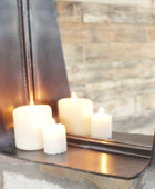 Candle holder with three candles in front of a mirror reflecting a stone wall.