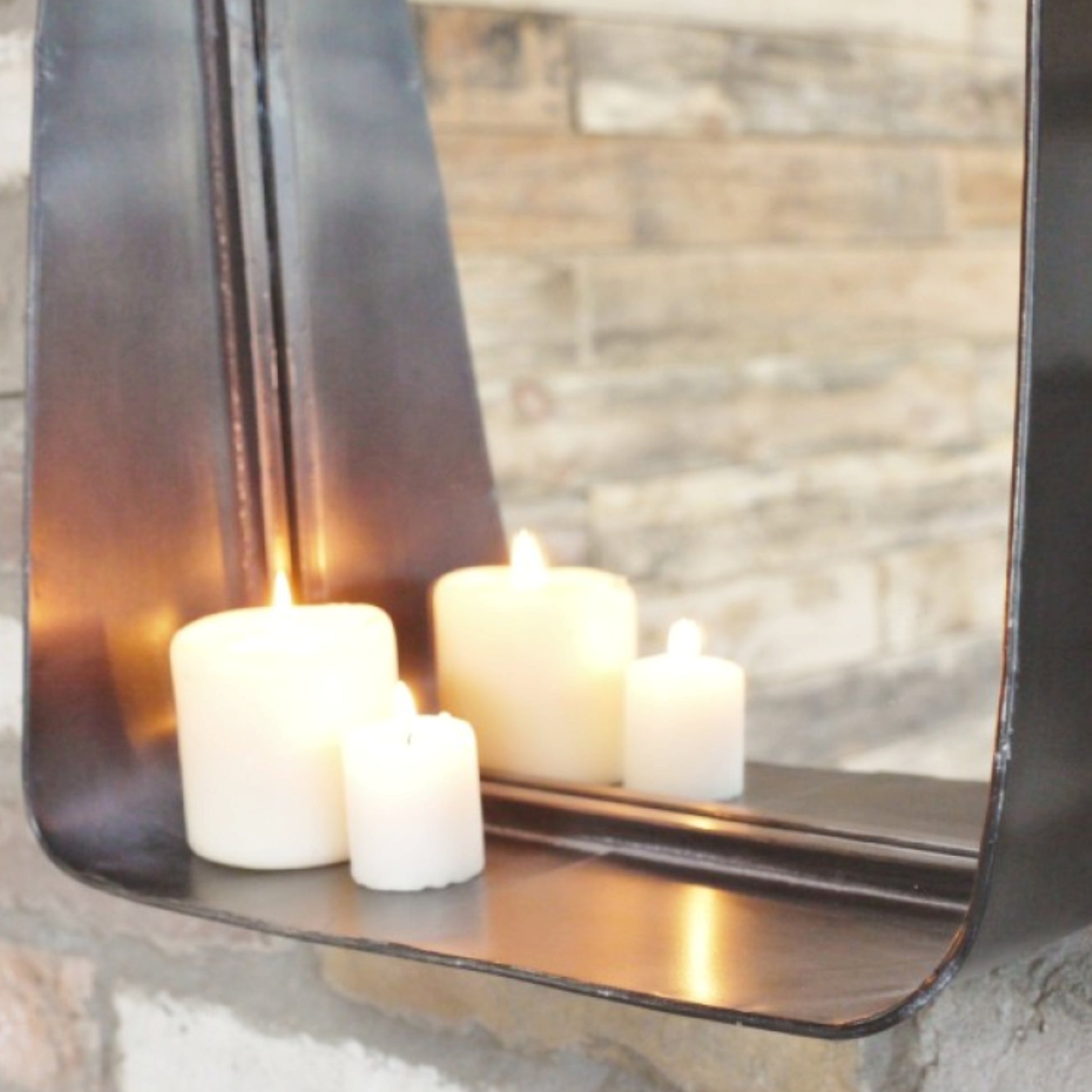 Candle holder with three candles in front of a mirror reflecting a stone wall.