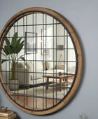 Round wall mirror with grid design on a gray wall, reflecting a living room.