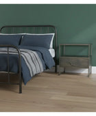 Bedroom with a metal bed frame, blue bedding, and a nightstand against a green wall.