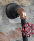 Decorative metal pipe with a red valve handle against a stone wall background