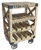 A rustic industrial-style wooden rolling cart with three tiers, featuring a top shelf as a small table, wine bottle slots on the middle and bottom tiers, and black metal corner brackets and stenciled text, shown on a wood floor against a gray wall.
