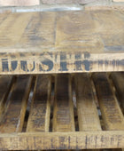 A rustic wooden pallet table or shelf made from weathered brown wood planks, with a dark stencil-style word printed across the front edge and slatted side panels.