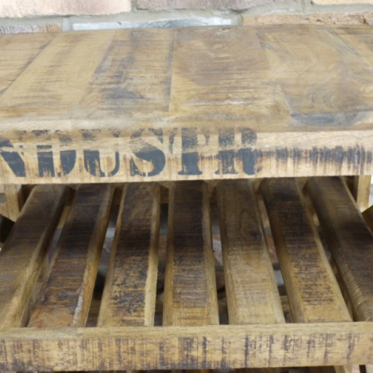 A rustic wooden pallet table or shelf made from weathered brown wood planks, with a dark stencil-style word printed across the front edge and slatted side panels.