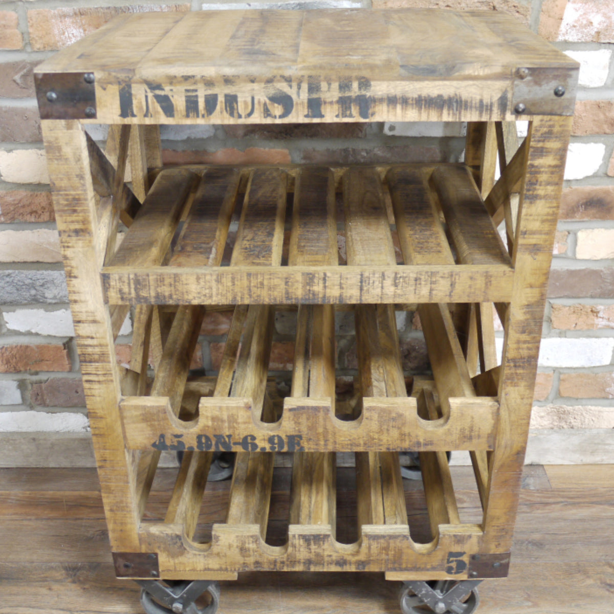 A rustic three-tier wooden rolling cart made from a pallet, featuring a slatted top, wine bottle holders on the middle and bottom tiers, and castor wheels. The wood has a weathered brown finish with black stenciled text.