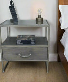 Metal nightstand with glass top, books, and a lamp on a wooden floor.