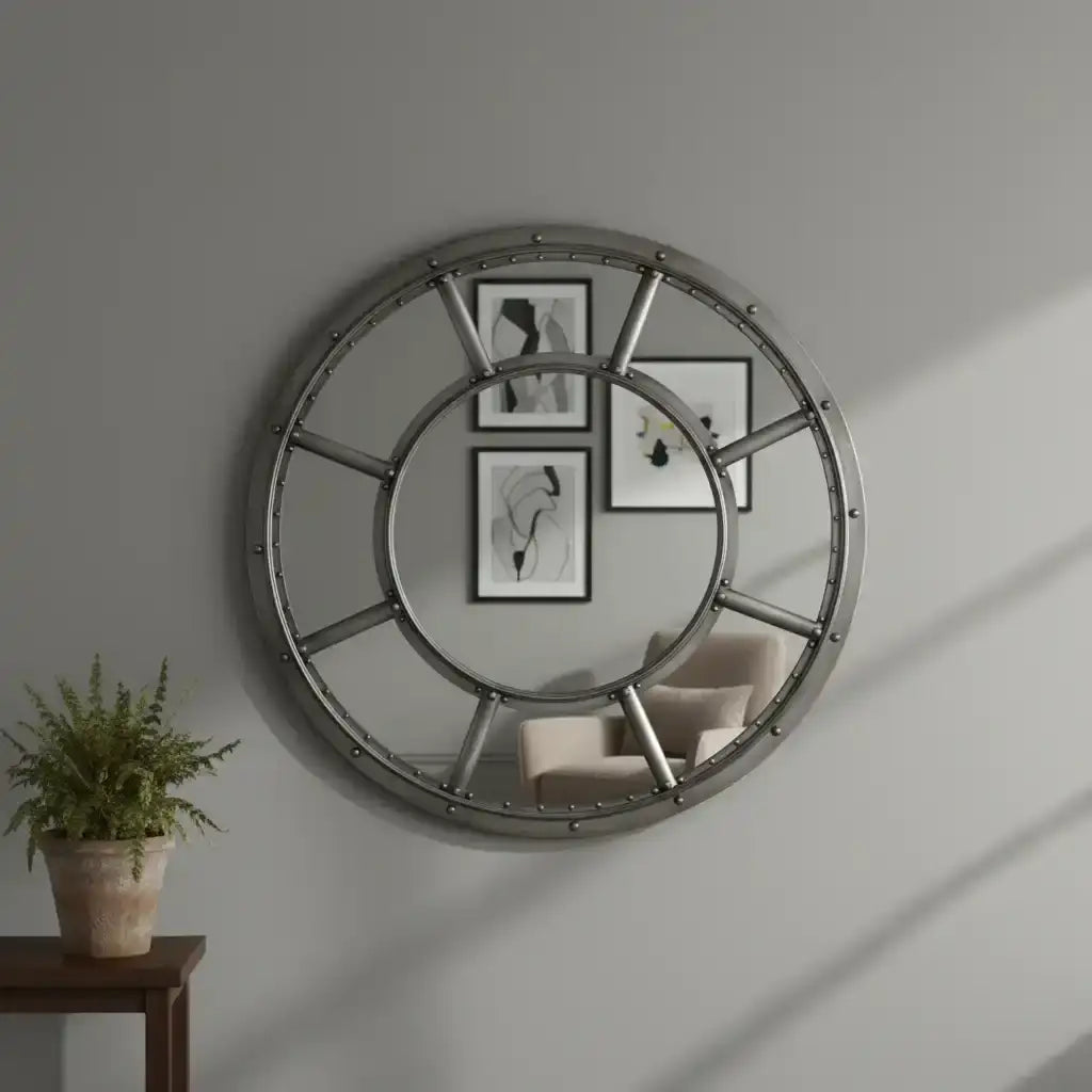 Round metallic wall mirror on a gray wall with a plant and chair in the foreground