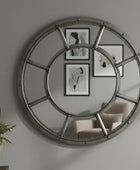 Large round mirror with metal frame on a wall with framed pictures and a chair.