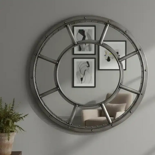 Large round mirror with metal frame on a wall with framed pictures and a chair.