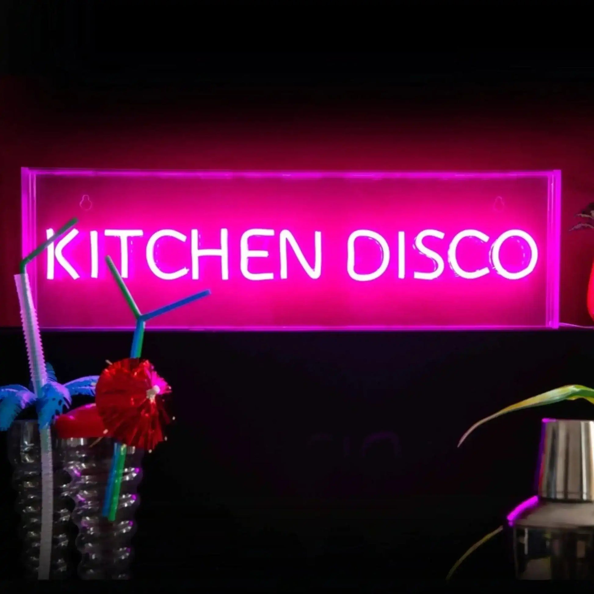 Neon sign reading 'KITCHEN DISCO' with decorative items on a dark background