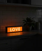 Orange LED sign displaying 'LOVE' on a kitchen counter with a plant and jars in the background.