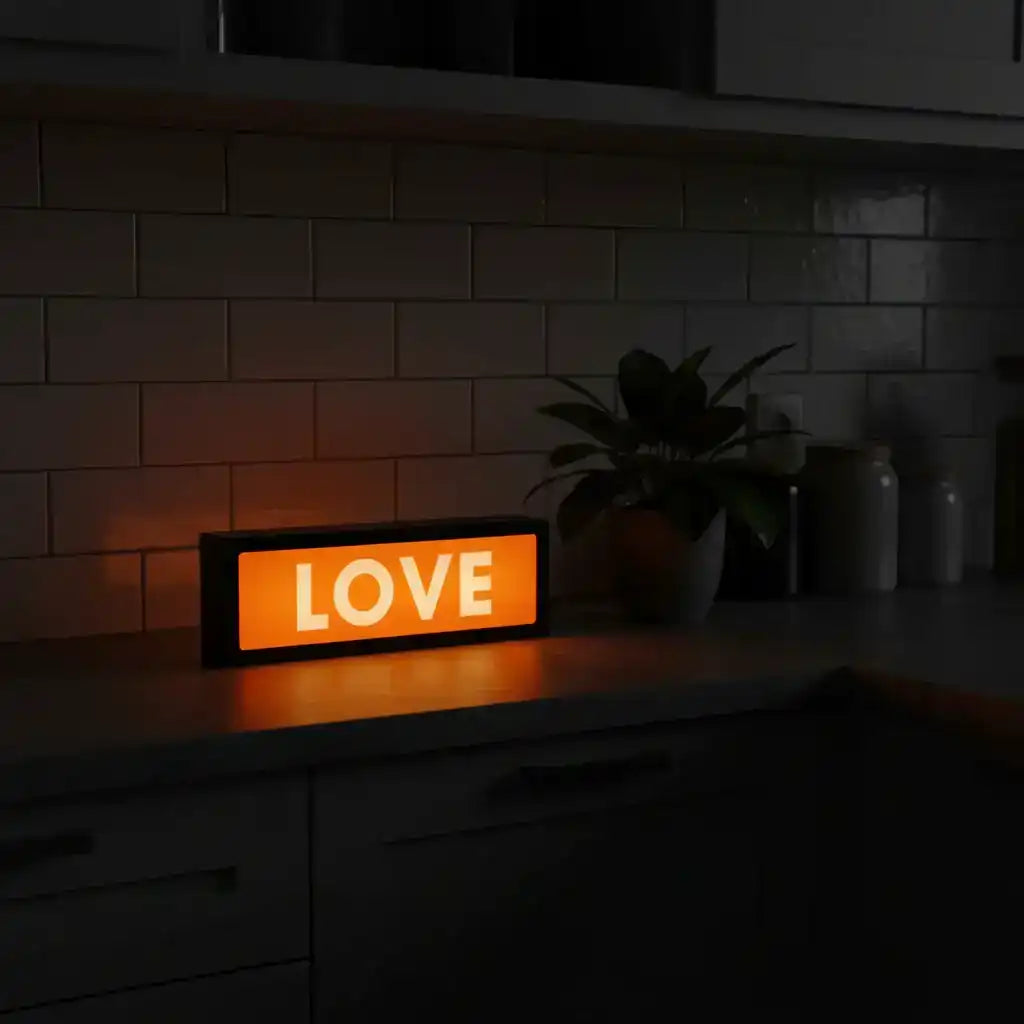Orange LED sign displaying 'LOVE' on a kitchen counter with a plant and jars in the background.