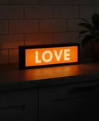 Orange LED sign with 'LOVE' text on a dark surface with a plant in the background.