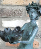 Bronze statue of a woman holding a flower against a stone wall background