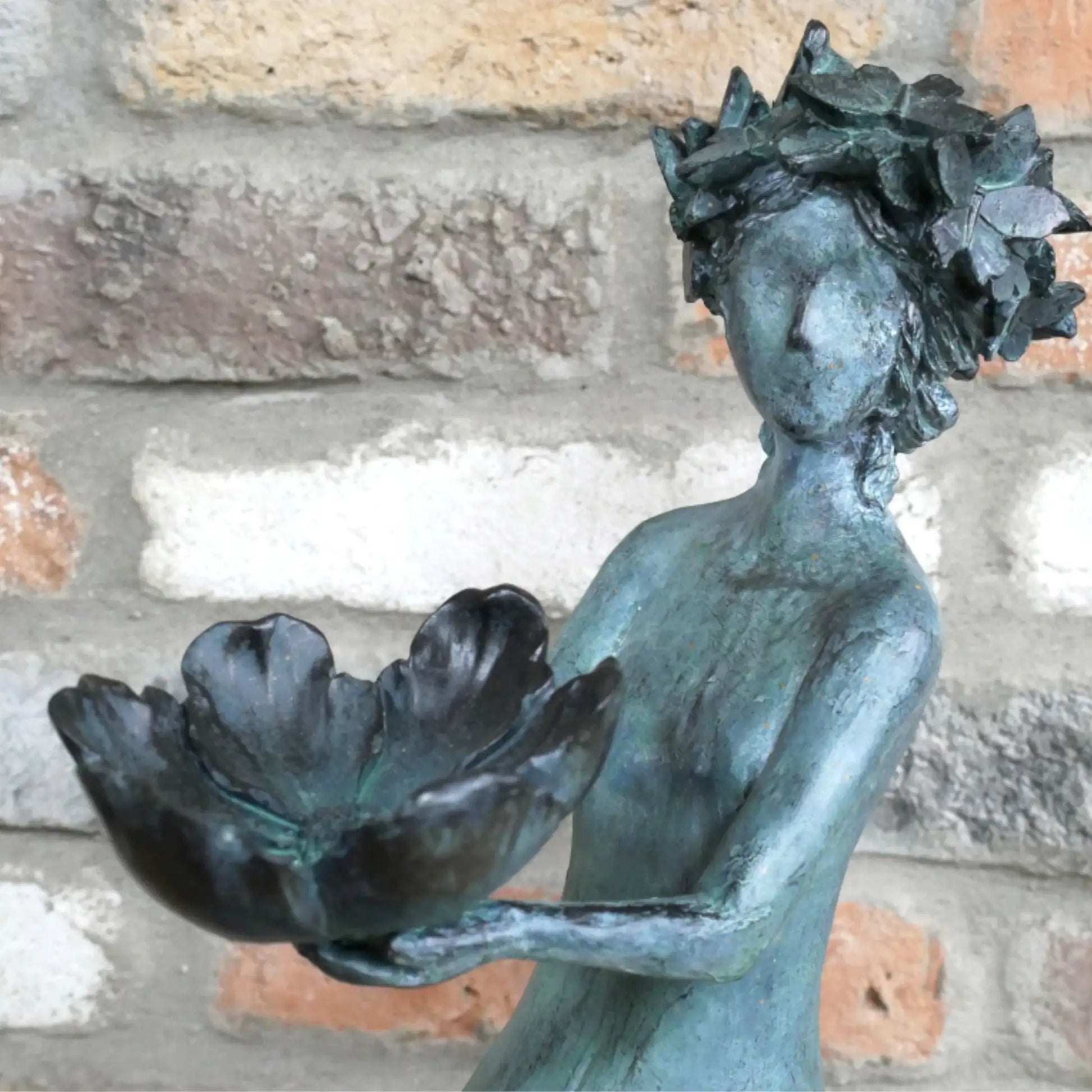Bronze statue of a woman holding a flower against a stone wall background