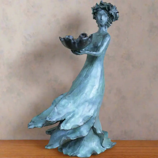 Bronze statue of a woman holding a lotus flower on a wooden surface with a beige background