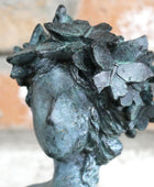 Bronze statue of a woman's head with leaves on her head against a blurred background