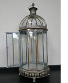 An ornate vintage-style birdcage lantern with a domed glass top, clear glass side panels, and an open side door, featuring an antique silver-toned metal frame and decorative base.