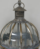 A close-up of an ornate vintage lantern with a clear ribbed glass dome, silver-toned metal frame, and decorative top finial against a neutral gray background.
