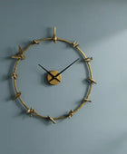 Decorative wall clock with gold branch design on a blue wall