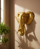Gold elephant head sculpture on a wall with a plant in the corner