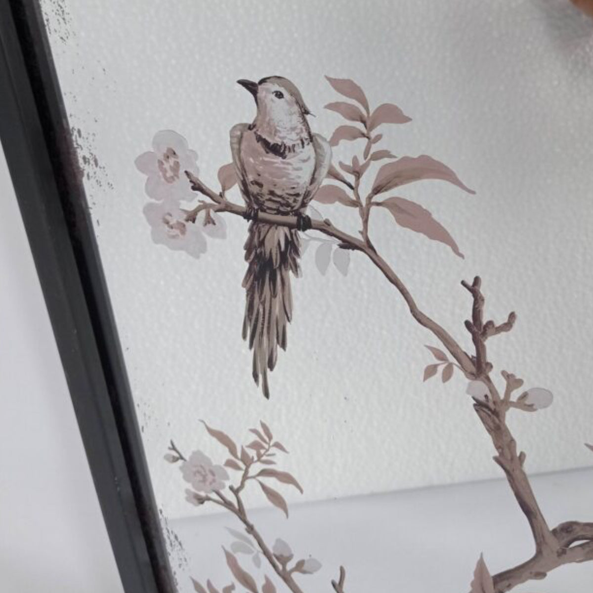A close-up of a framed wall art print featuring a small bird perched on a branch with pale blossoms, shown against a white textured background.