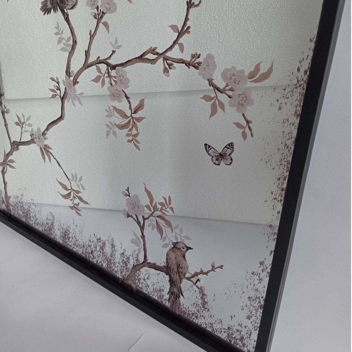 A framed wall art print featuring delicate cherry blossom branches with pale pink flowers, brown leaves, birds perched on branches, and a butterfly on an off-white background.