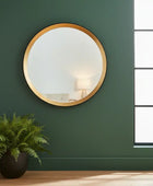 Round gold-framed mirror on a green wall with a potted plant below.